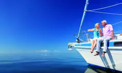 Happy senior couple sitting on the bow of a sail boat on a calm blue sea