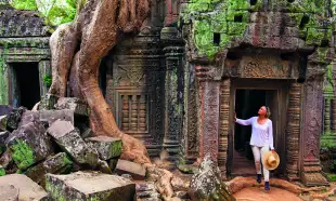 A Woman paused in the doorway of an ancient ruin of Ta Prohm, looking in up in admiration.