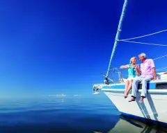 Happy senior couple sitting on the bow of a sail boat on a calm blue sea